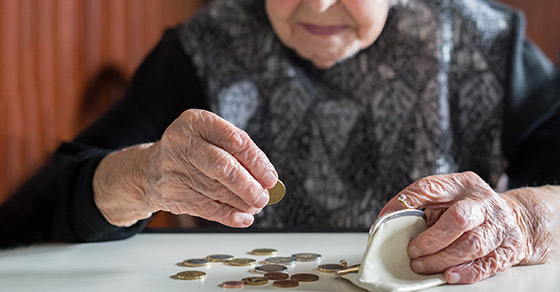 Elderly woman sitting at the table counting money in her wallet.